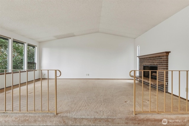 empty room with lofted ceiling, a textured ceiling, a brick fireplace, and carpet flooring