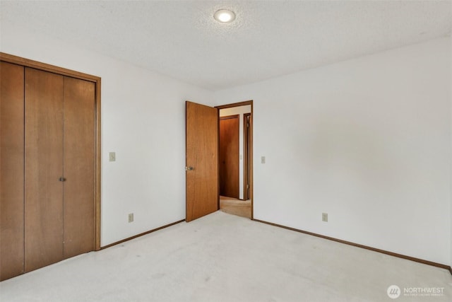 unfurnished bedroom featuring a textured ceiling, baseboards, a closet, and light carpet