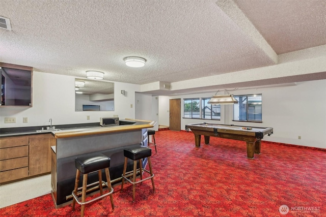 kitchen with brown cabinetry, visible vents, a breakfast bar, a sink, and dark carpet