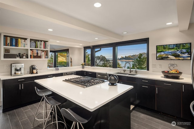 kitchen with dark cabinets, a kitchen island, a sink, a kitchen breakfast bar, and light countertops