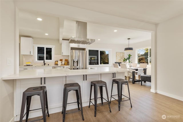 kitchen with pendant lighting, white cabinets, stainless steel fridge, a kitchen bar, and island exhaust hood