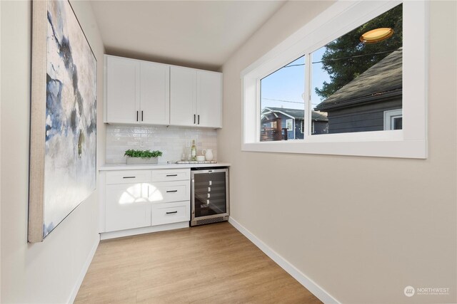 bar featuring backsplash, wine cooler, white cabinetry, and light wood-type flooring