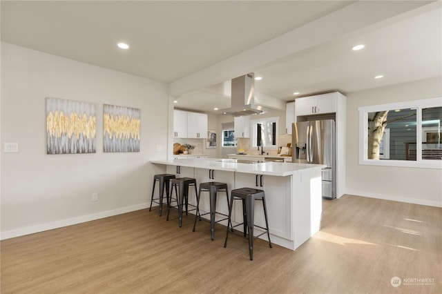 kitchen featuring white cabinetry, kitchen peninsula, stainless steel fridge, island exhaust hood, and a breakfast bar area