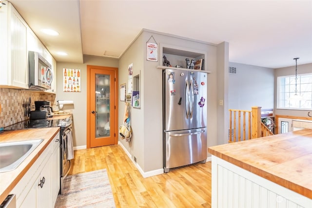 kitchen with wooden counters, light hardwood / wood-style flooring, appliances with stainless steel finishes, decorative light fixtures, and white cabinetry