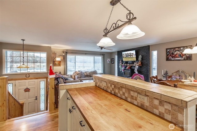 kitchen with a ceiling fan, wood counters, open floor plan, hanging light fixtures, and light wood-type flooring