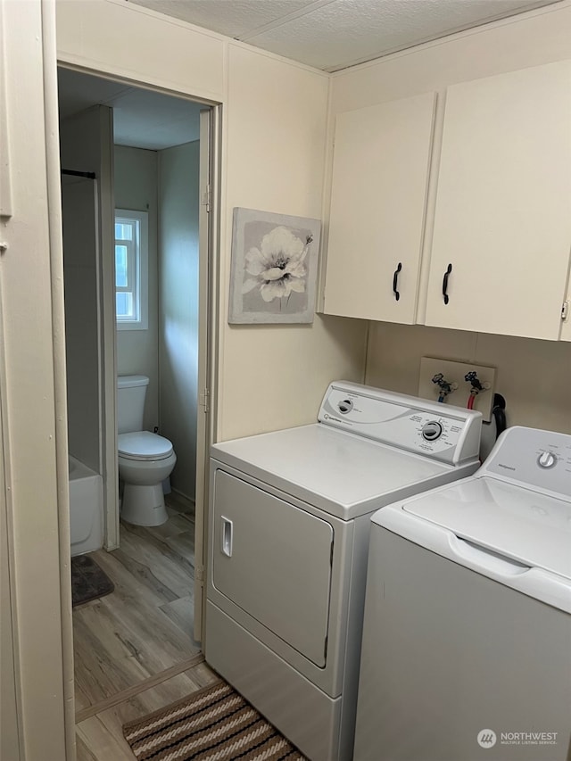 clothes washing area featuring washer and dryer, light hardwood / wood-style floors, cabinets, and a textured ceiling