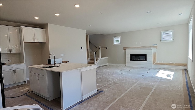 kitchen featuring a sink, a glass covered fireplace, recessed lighting, tasteful backsplash, and a center island with sink