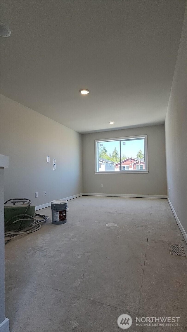 empty room with unfinished concrete floors, baseboards, and visible vents