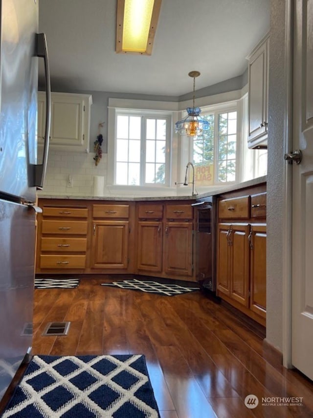 kitchen with appliances with stainless steel finishes, tasteful backsplash, dark wood-type flooring, pendant lighting, and a notable chandelier