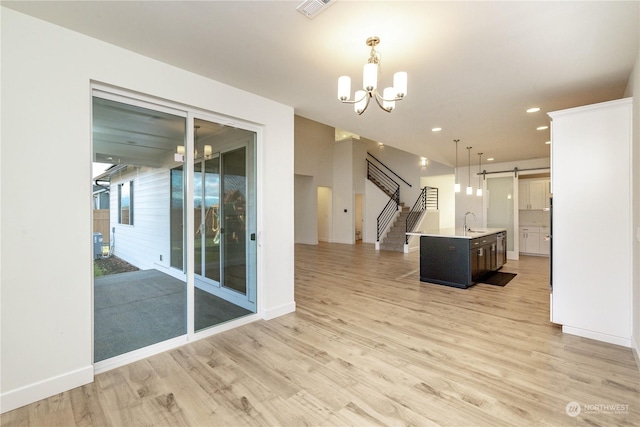 interior space featuring a barn door, light wood-style flooring, stairway, an inviting chandelier, and a sink