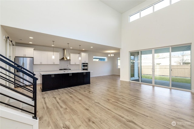 kitchen with a center island with sink, light countertops, open floor plan, wall chimney range hood, and light wood-type flooring