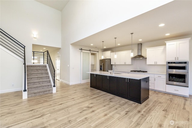 kitchen featuring a barn door, a sink, light countertops, wall chimney range hood, and appliances with stainless steel finishes