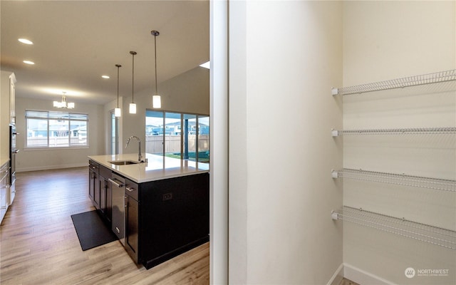 kitchen featuring sink, hanging light fixtures, stainless steel dishwasher, a chandelier, and light hardwood / wood-style floors