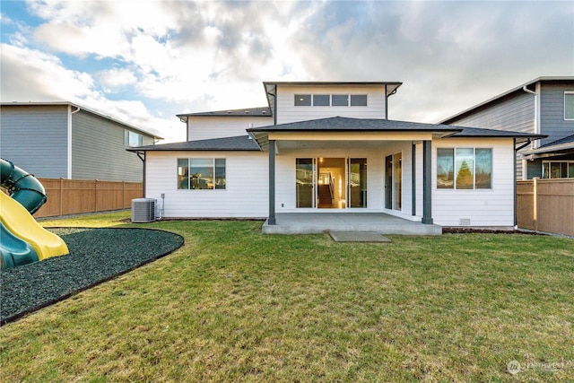 rear view of property with a playground, a yard, central AC unit, a patio area, and a fenced backyard