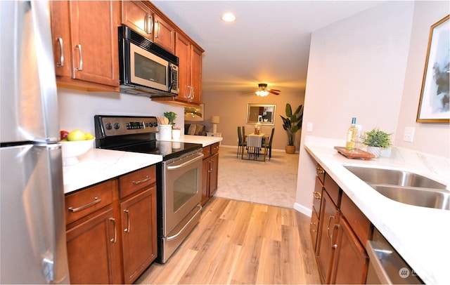 kitchen with sink, light stone counters, light hardwood / wood-style flooring, appliances with stainless steel finishes, and ceiling fan