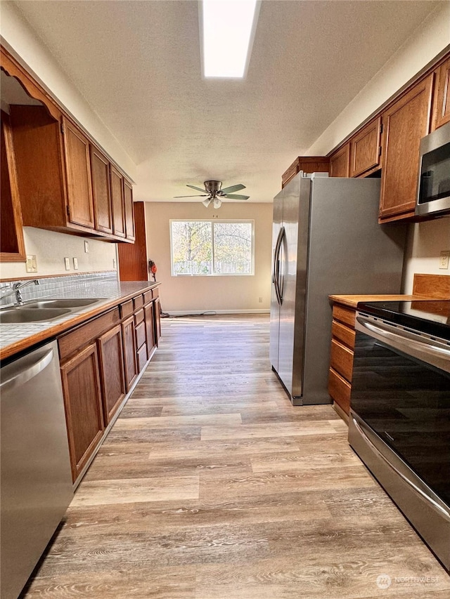 kitchen featuring appliances with stainless steel finishes, a textured ceiling, ceiling fan, sink, and light hardwood / wood-style floors