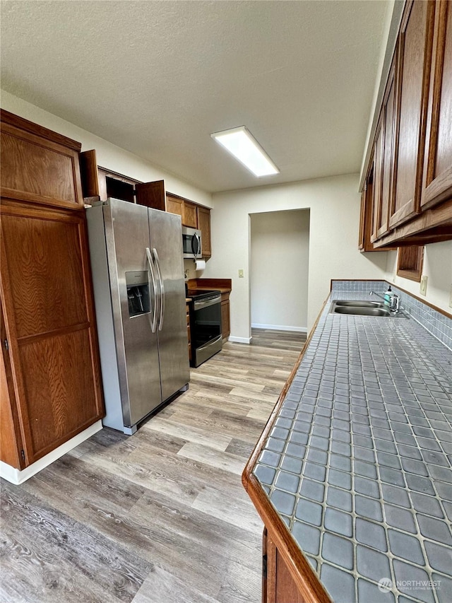 kitchen featuring a textured ceiling, stainless steel appliances, sink, light hardwood / wood-style flooring, and tile counters