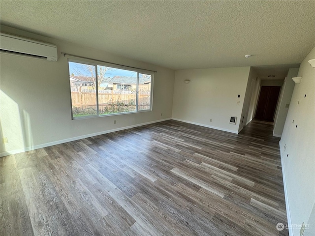 spare room with a textured ceiling, dark hardwood / wood-style floors, and a wall unit AC