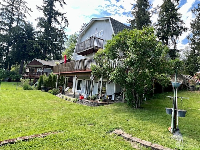 rear view of house with a balcony, a wooden deck, a yard, and a patio