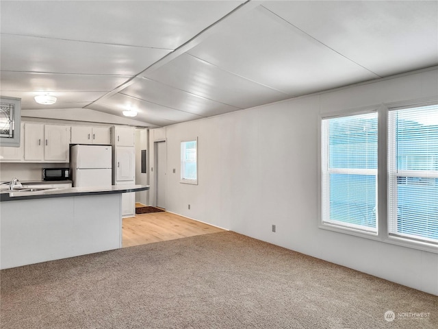 kitchen with white cabinets, white refrigerator, sink, vaulted ceiling, and light wood-type flooring