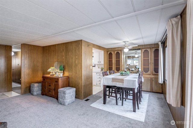 carpeted dining space with ceiling fan and wood walls