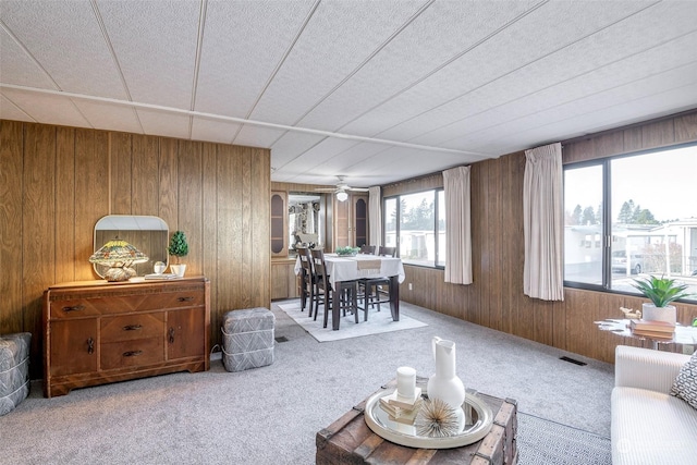 carpeted living room with ceiling fan and wooden walls