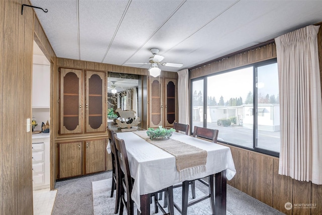 dining room featuring ceiling fan, wood walls, and a textured ceiling