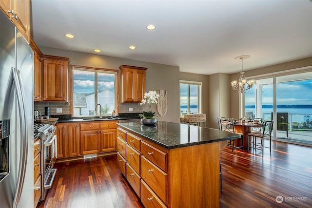 kitchen featuring an inviting chandelier, tasteful backsplash, a kitchen island, a water view, and appliances with stainless steel finishes