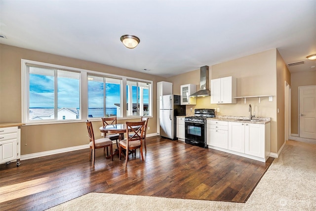 kitchen with stainless steel refrigerator, white cabinetry, wall chimney range hood, black range with gas stovetop, and dark hardwood / wood-style flooring