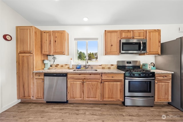 kitchen with light stone countertops, sink, wood-type flooring, and stainless steel appliances