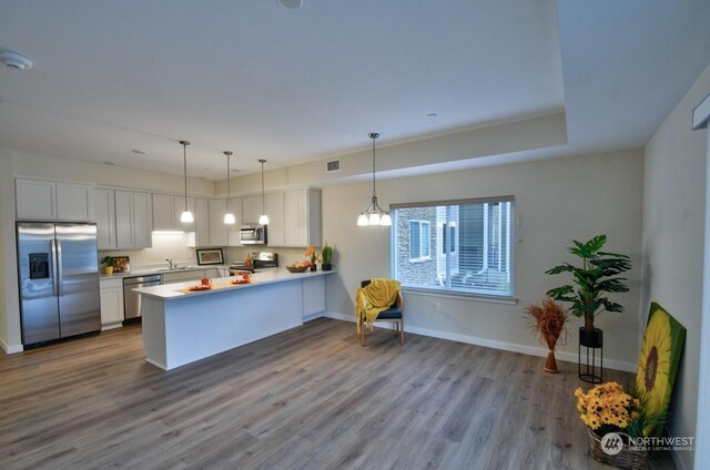 kitchen with light hardwood / wood-style floors, appliances with stainless steel finishes, white cabinetry, decorative light fixtures, and kitchen peninsula