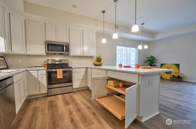 kitchen featuring pendant lighting, appliances with stainless steel finishes, white cabinetry, kitchen peninsula, and light wood-type flooring