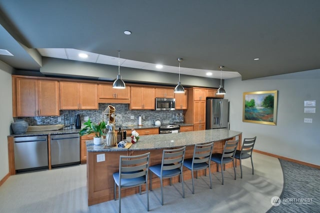 kitchen with pendant lighting, appliances with stainless steel finishes, a kitchen bar, a center island, and stone counters