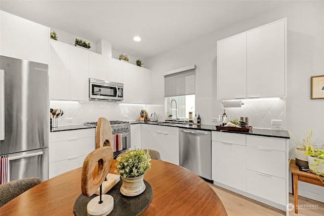 kitchen with white cabinets, sink, tasteful backsplash, light hardwood / wood-style floors, and stainless steel appliances