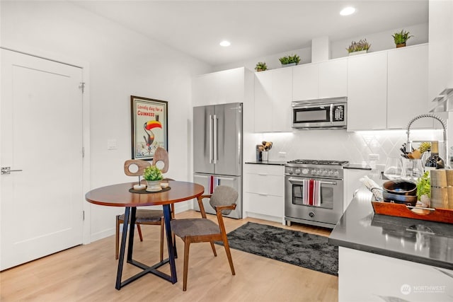 kitchen featuring white cabinets, backsplash, appliances with stainless steel finishes, and light hardwood / wood-style flooring