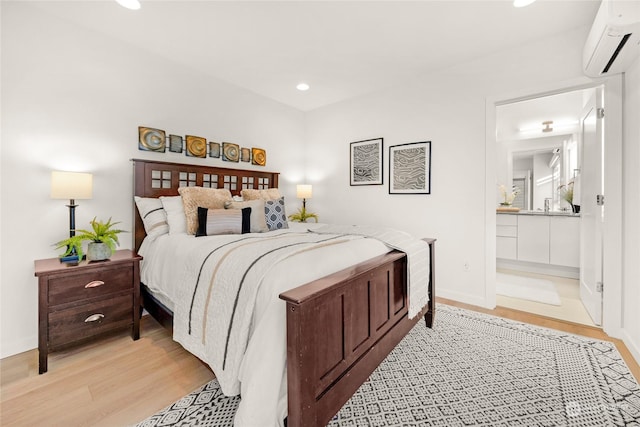 bedroom with connected bathroom, light hardwood / wood-style floors, and a wall unit AC