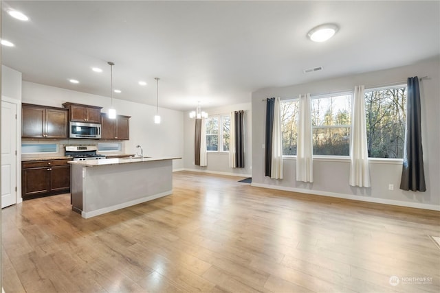 kitchen featuring sink, appliances with stainless steel finishes, a kitchen island with sink, pendant lighting, and light hardwood / wood-style floors