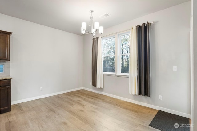 unfurnished dining area with a notable chandelier and light hardwood / wood-style flooring