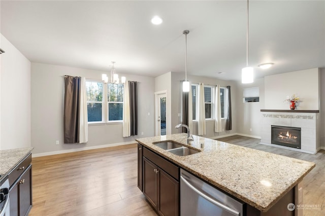 kitchen with sink, a kitchen island with sink, light stone countertops, decorative light fixtures, and stainless steel dishwasher