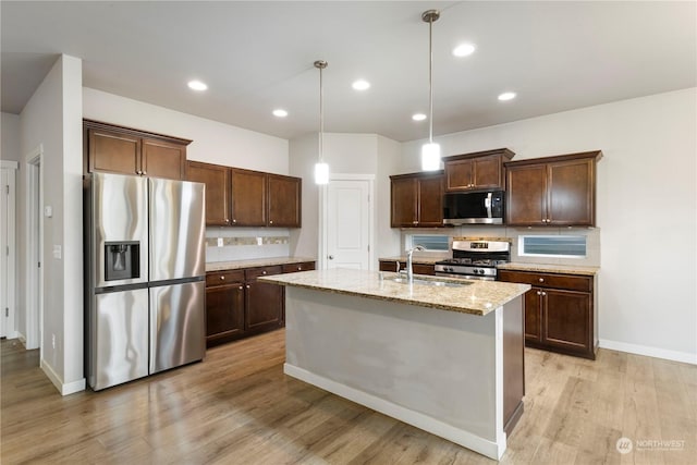 kitchen with sink, decorative light fixtures, light stone countertops, a kitchen island with sink, and stainless steel appliances