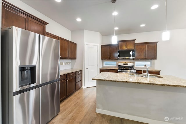 kitchen featuring pendant lighting, appliances with stainless steel finishes, dark brown cabinetry, light stone countertops, and light hardwood / wood-style floors