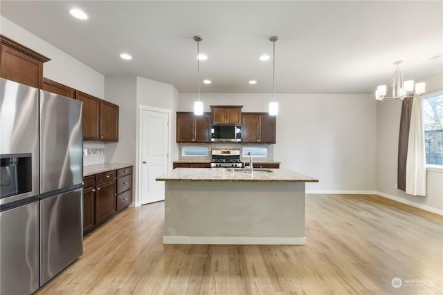 kitchen with hanging light fixtures, a center island with sink, stainless steel appliances, and light hardwood / wood-style flooring