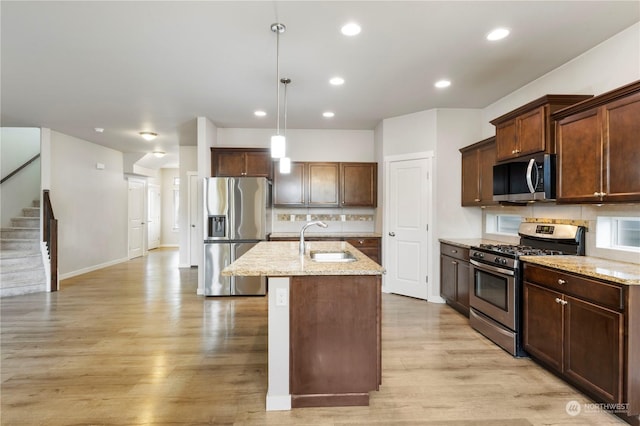 kitchen featuring sink, appliances with stainless steel finishes, hanging light fixtures, light hardwood / wood-style floors, and an island with sink