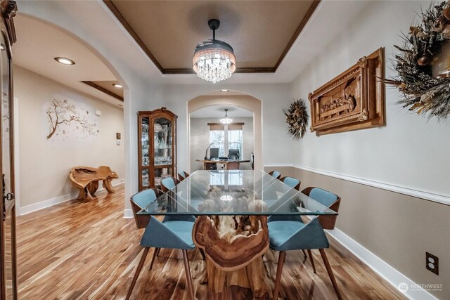 dining area with a chandelier, a raised ceiling, and light hardwood / wood-style flooring