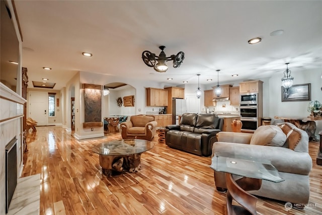 living room with ceiling fan with notable chandelier, light wood-type flooring, and a tiled fireplace