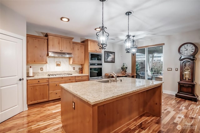 kitchen featuring appliances with stainless steel finishes, light stone counters, a kitchen island with sink, sink, and light hardwood / wood-style flooring