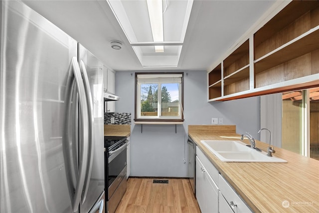 kitchen with decorative backsplash, appliances with stainless steel finishes, sink, light hardwood / wood-style flooring, and white cabinetry