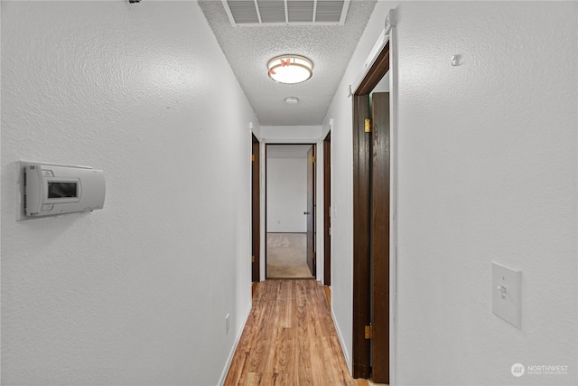 corridor featuring a textured ceiling and light hardwood / wood-style flooring