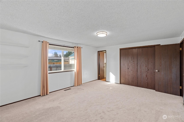 unfurnished bedroom featuring light colored carpet, a textured ceiling, and a closet