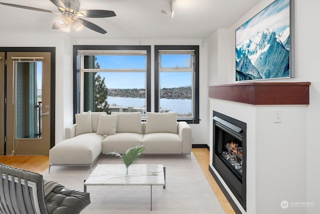 living room featuring ceiling fan, a water view, and light hardwood / wood-style flooring